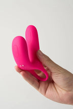 Pink Myvelvettouch Cock Ring and Remote Control Couple Vibrator held in a hand against a light gray background