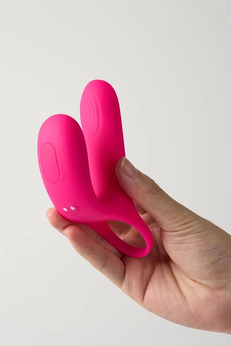 Pink Myvelvettouch Cock Ring and Remote Control Couple Vibrator held in a hand against a light gray background