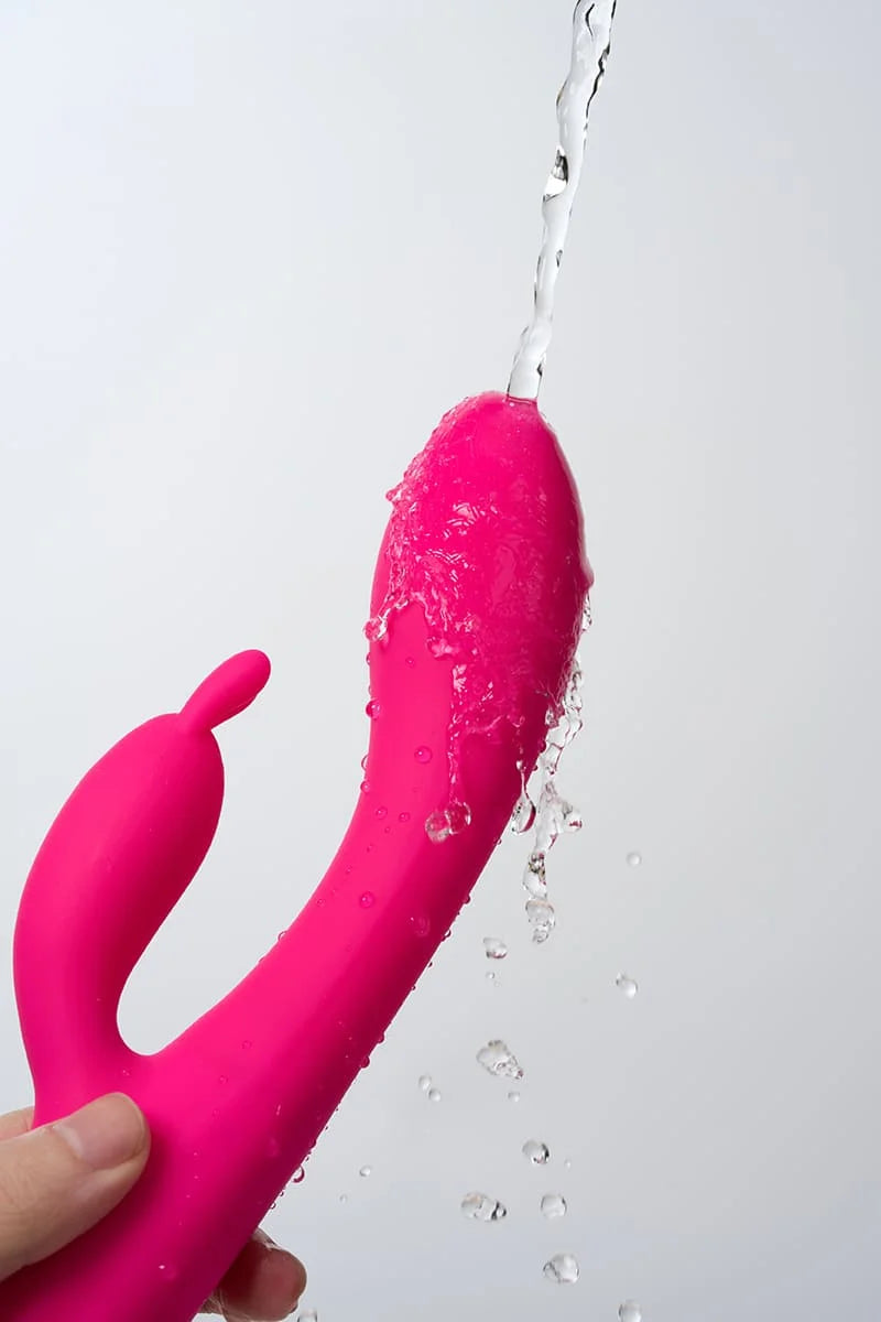 Pink Myvelvettouch Heated Rabbit Vibrator with water being sprayed on a white background