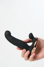 Hand holding a black and gold Myvelvettouch Men's Prostate Vibrator with Remote Control against a white background