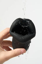 Black silicone Myvelvettouch Penis Trainer being held with water dripping from it on a light gray background