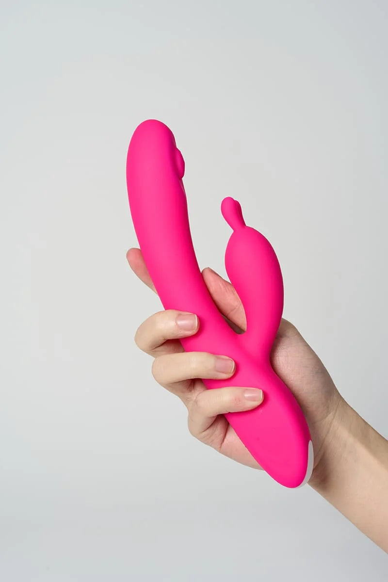 Hand holding a pink Myvelvettouch Rabbit Clitoral Stimulation and G-spot Slapping Vibrator against a light gray background