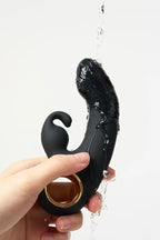 Black and gold Myvelvettouch Rabbit Clitoral Stimulator and Finger G-spot Vibrator Massager held by a hand with water droplets on a white background