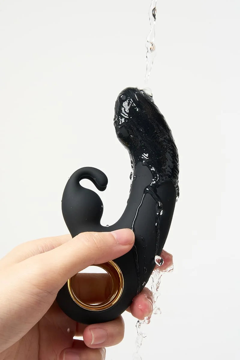 Black and gold Myvelvettouch Rabbit Clitoral Stimulator and Finger G-spot Vibrator Massager held by a hand with water droplets on a white background