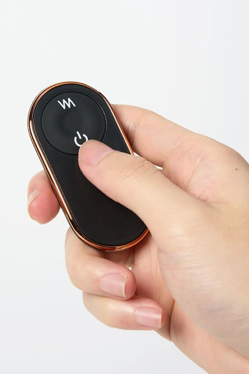 Hand holding a black remote control with copper accents of Myvelvettouch Rabbit Couple Vibrating Cock Ring on a white background