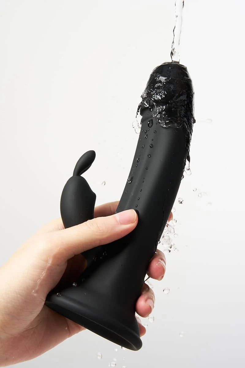 Black Myvelvettouch Rabbit Suction Cup Dildo held by a hand with water spraying onto it against a white background