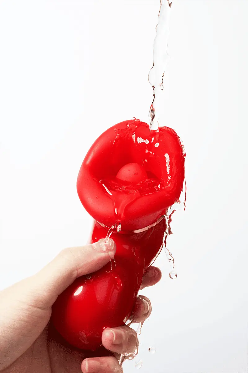 Myvelvettouch Sexy Red Lips Sucking Tongue Licking Vibrator being held with water dripping from it on a white background