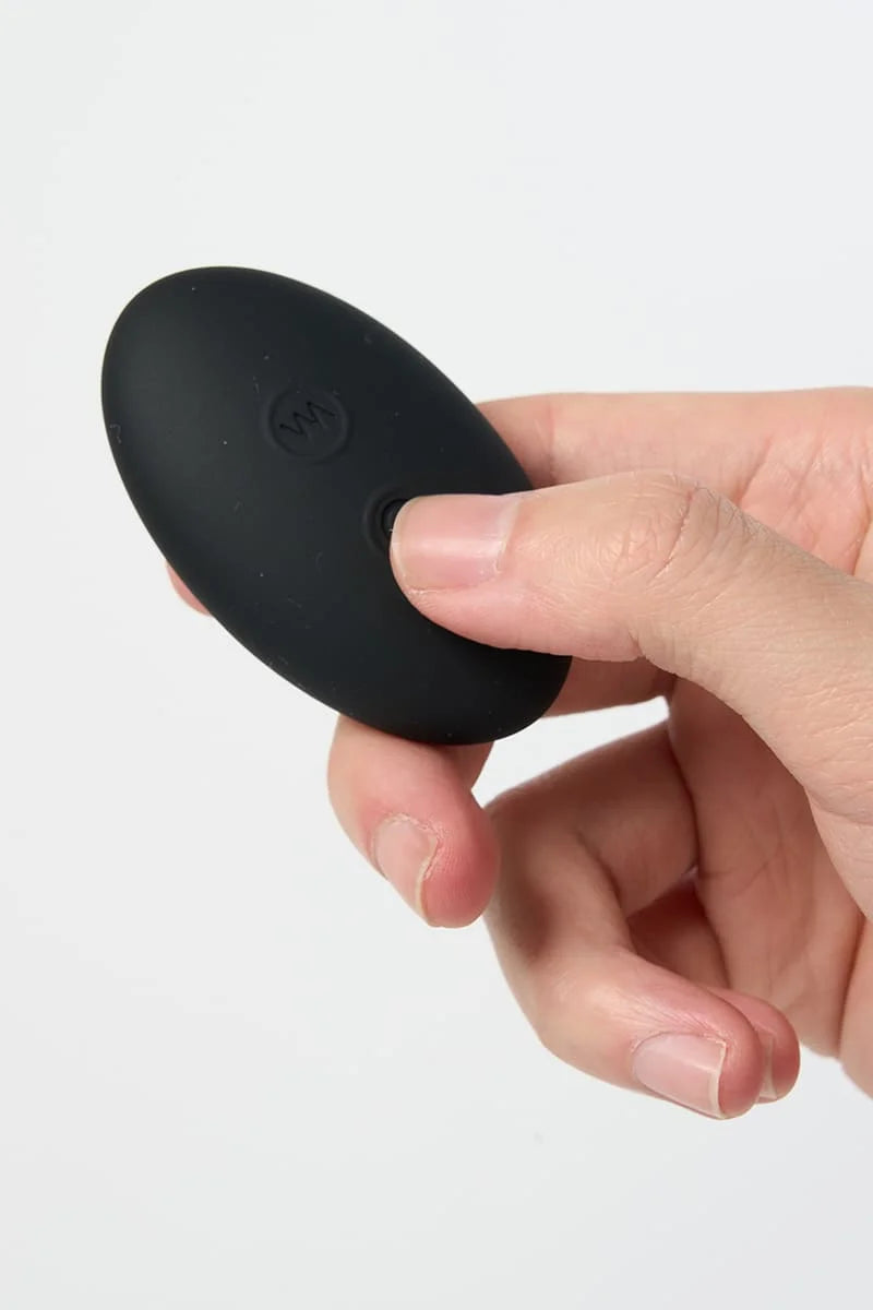 Hand holding a black silicone remote control of Myvelvettouch Unisex Prostate Vibrator on a white background