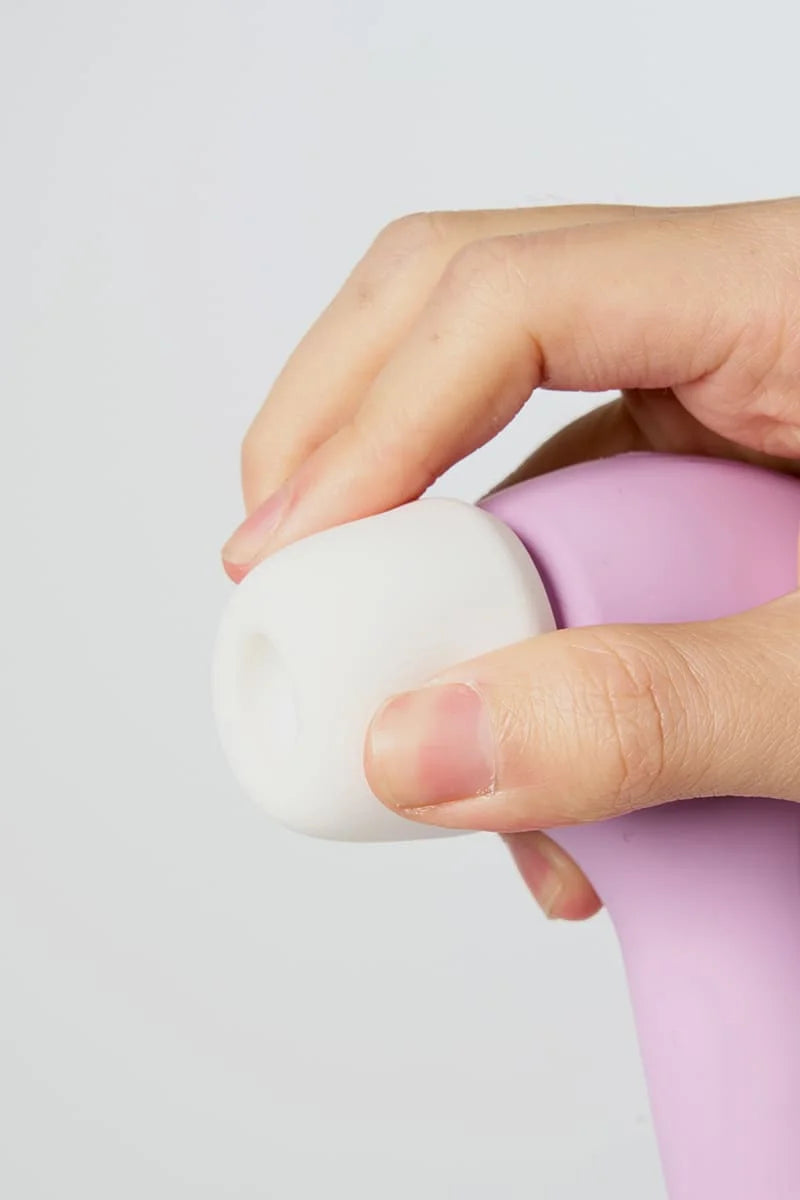 Hand holding a white and pink Myvelvettouch Rabbit 3-in-1 Tapping and Sucking Vibrator against a light gray background