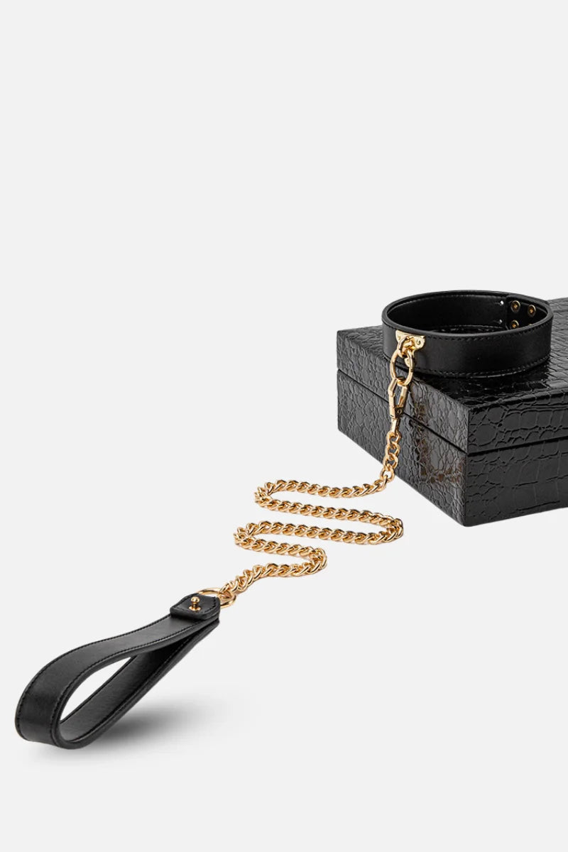 Black leather strap with gold chain and black container on a white background