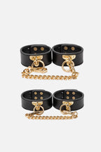 Black leather cuffs with gold chains on a white background