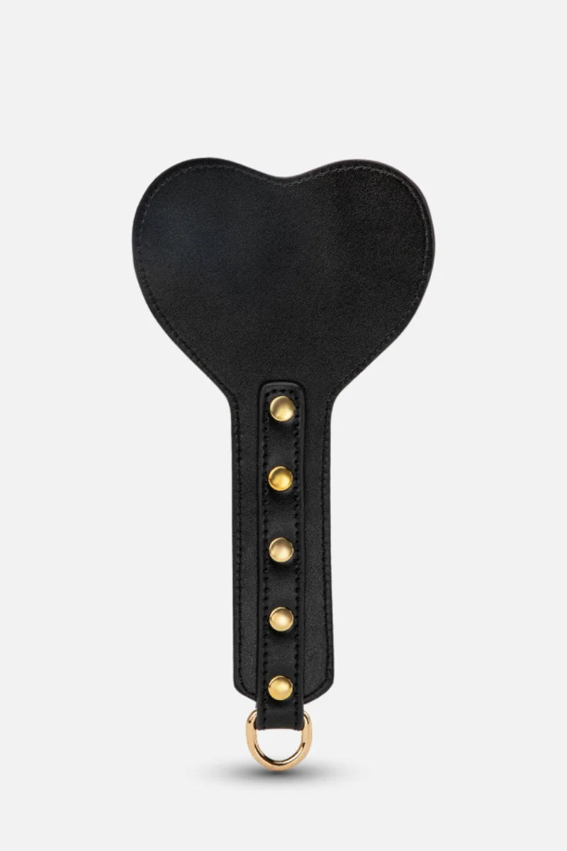 Black leather paddle with gold studs and ring on a white background