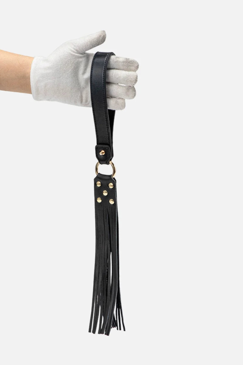 Black leather strap with tassels held by a gloved hand on a white background